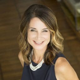 Smiling woman with wavy hair and a pearl necklace.