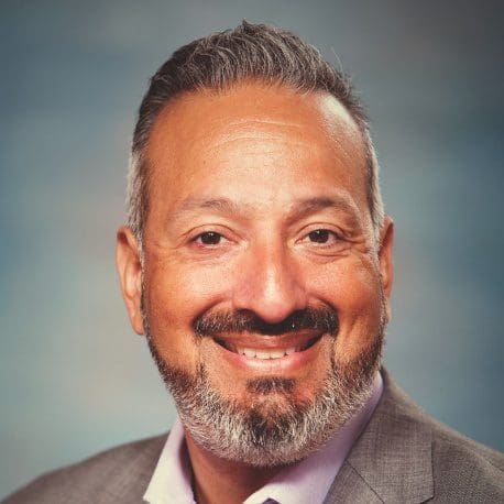 Smiling middle-aged man in a suit with a gray beard and mustache.