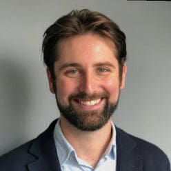 Smiling man with beard and suit jacket against a plain background.